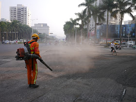 bicyclist going through a cloud of dust caused by a man blowing graving on a street in Zhuhai