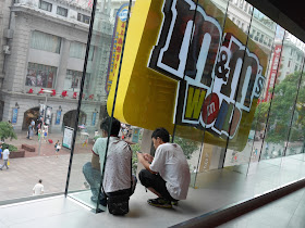 two young men staring out a window while crouched at the M&M's World in Shanghai
