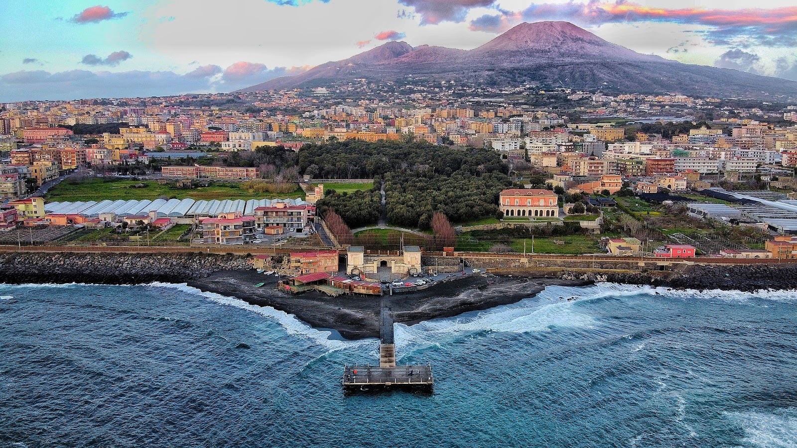 naples dramatic coast small pier sunset skyline traditional buildings mount vesuvius in background italy. Naples is a must-visit city on a Southern Italy road trip.