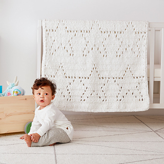 baby sitting in front of a white blanket with stars draped over a crib
