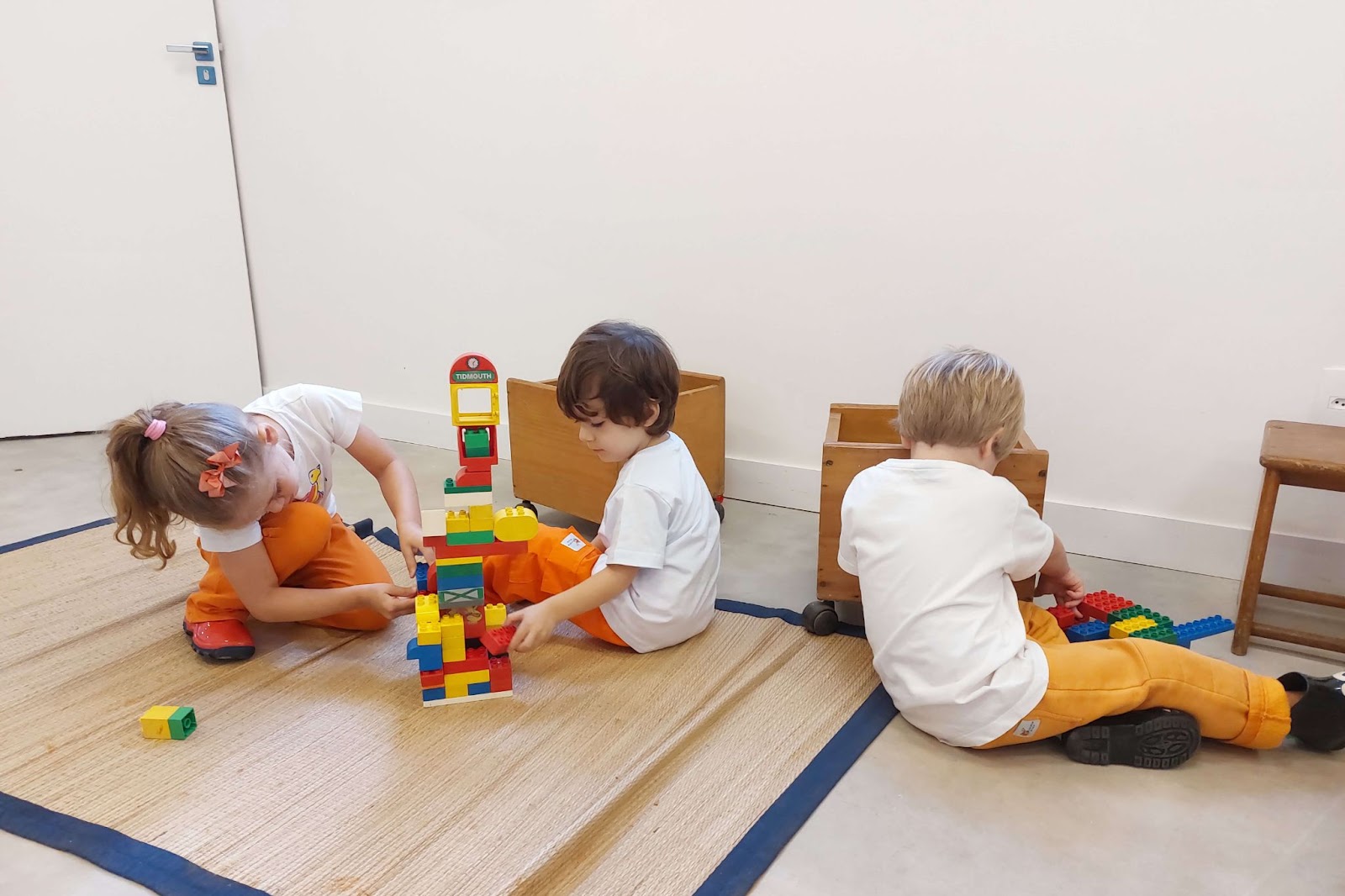 A imagem mostra 3 crianças brincando com um brinquedo de peças de montar coloridas.