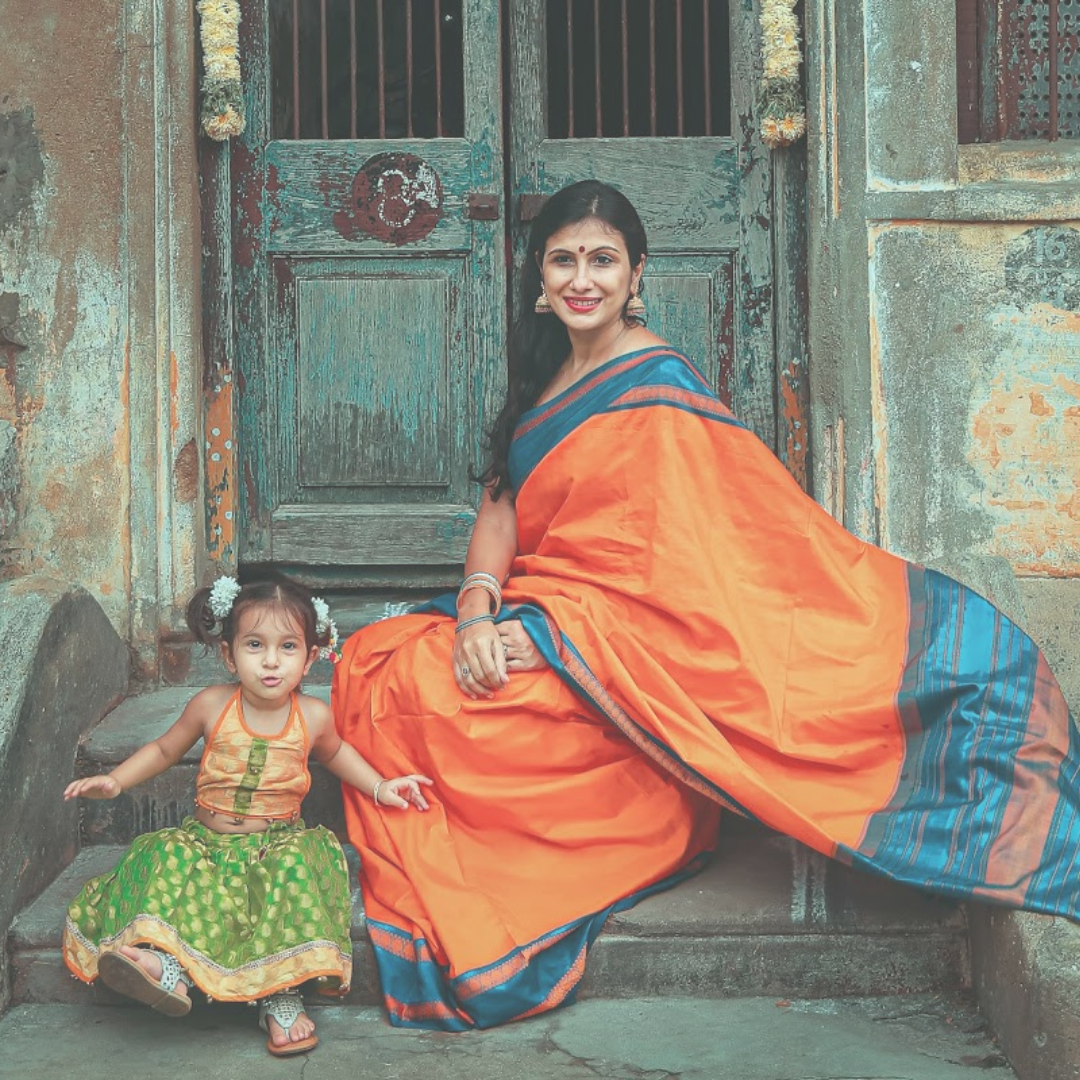 A mother with her daughter wearing orange dresses in the front of the temple