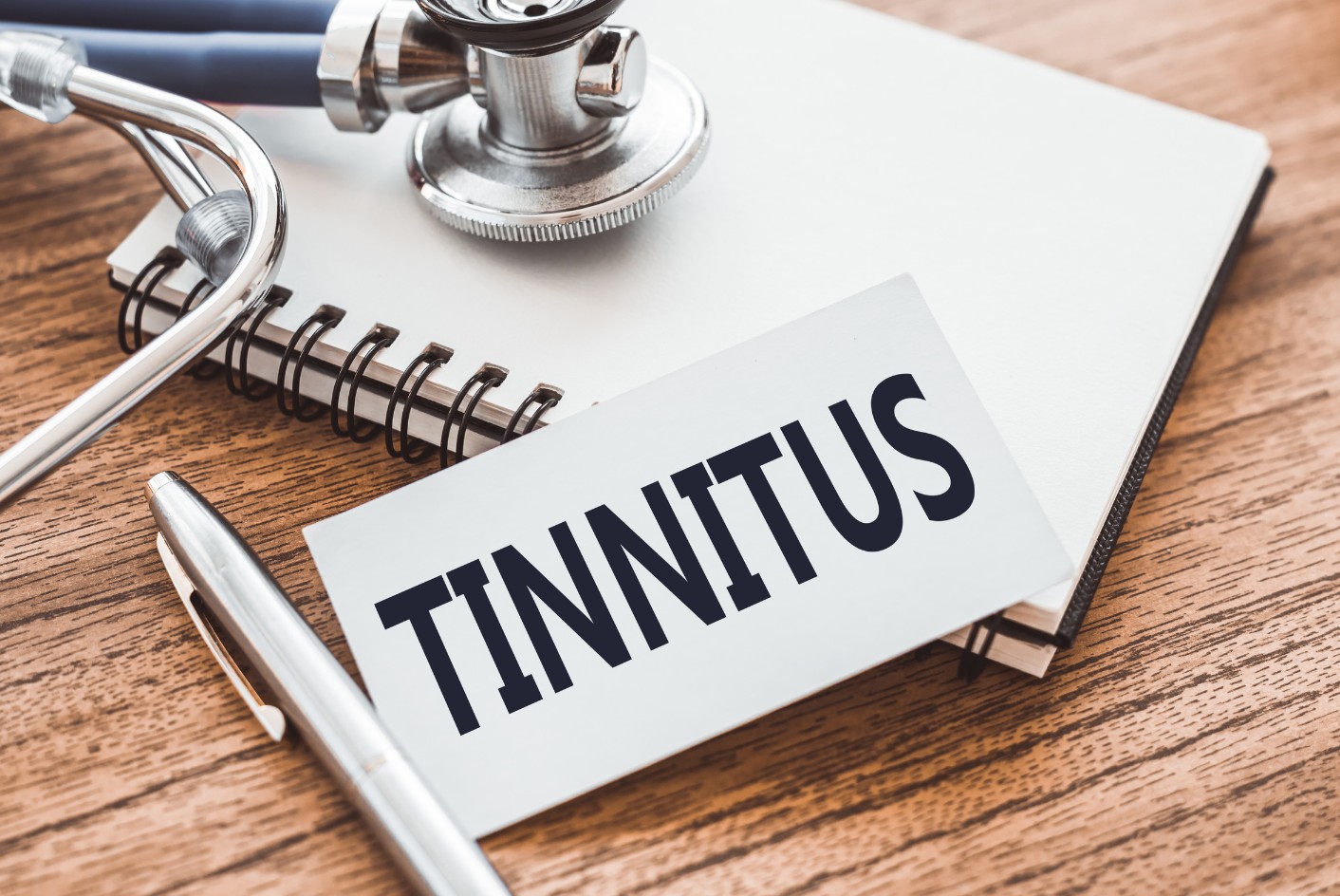 A piece of paper is on an office desk with the word, 'Tinnitus' printed on it in black.