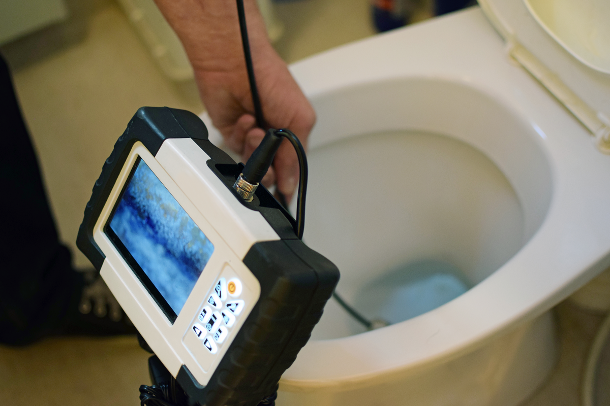 Plumber inserting sewer inspection camera in the toilet to locate the sewer clog.