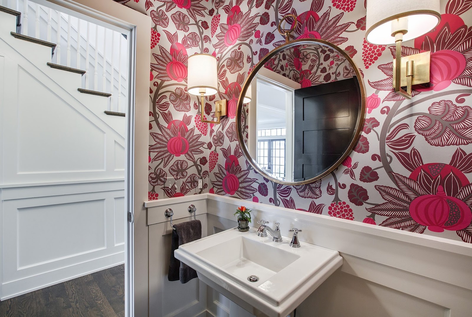 A bathroom with a circular mirror, pedestal sink, and colorful floral walls