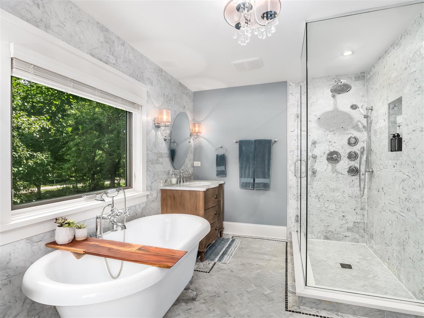Elegant master bath with a clawfoot soaking tub under a large picture window with a vanity and large glass surround shower