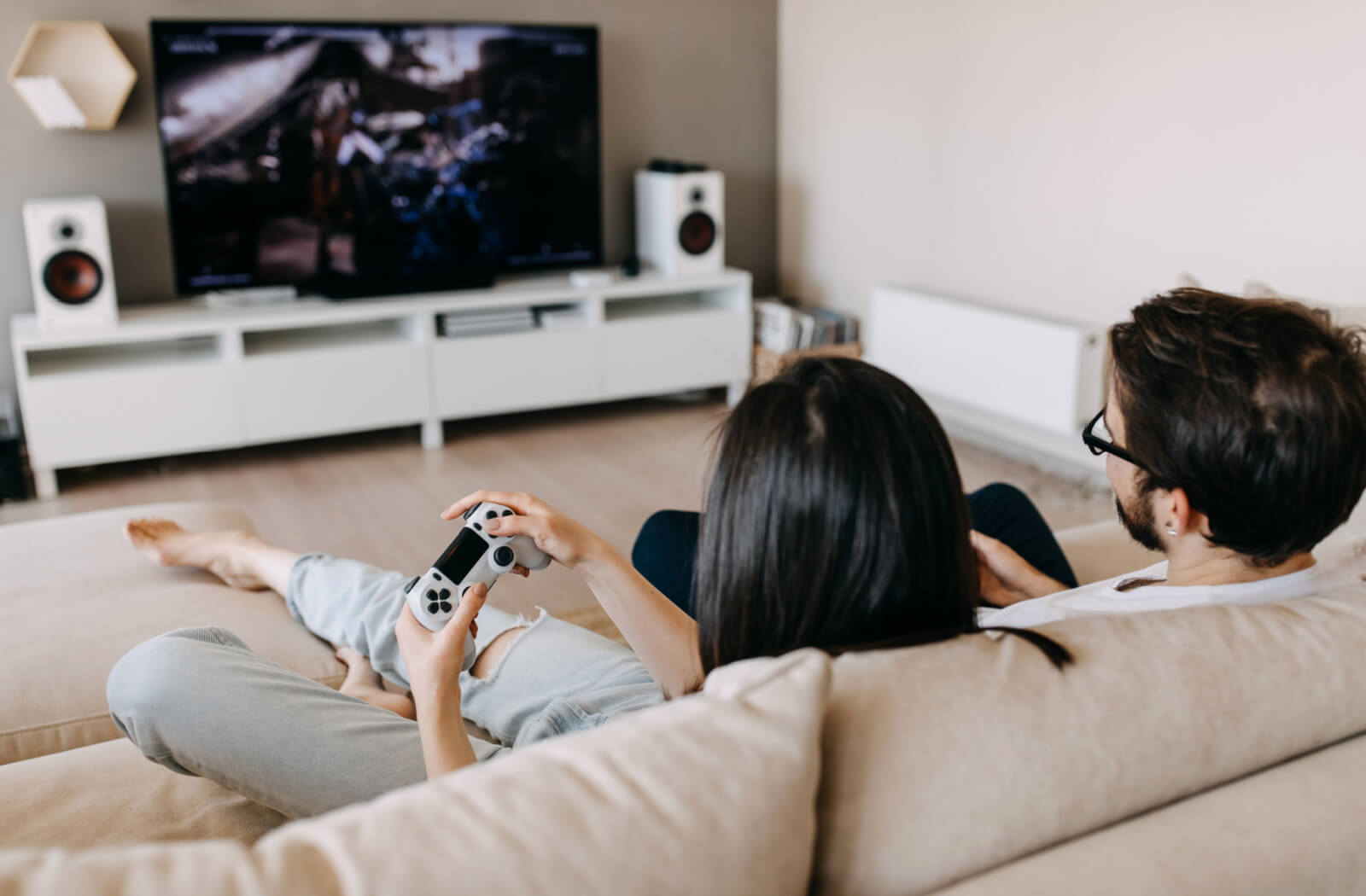 A couple sitting on a couch is playing video games away from the TV and taking screen breaks every 20 minutes to follow the 20-20-20 rule