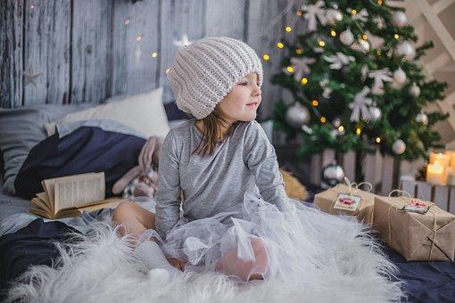 Small girl sitting on fluffy blanket with Christmas tree in the background, looking at gifts. 