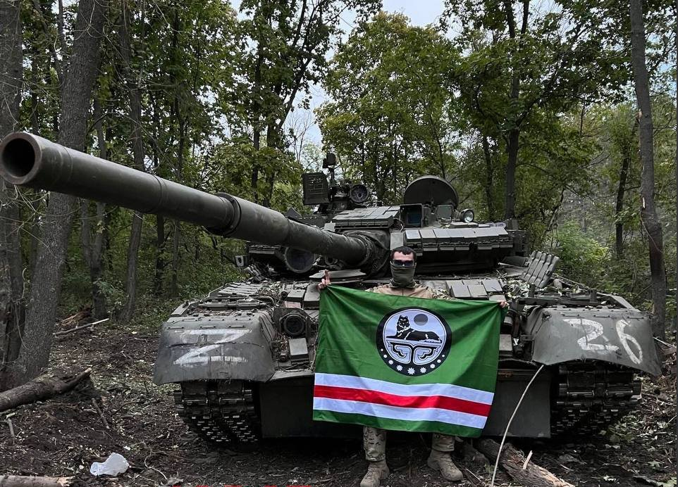 Dzokhar Dudayev fighter posing in front of a T-80 tank in Kharkiv Oblast holding an Ichkerian flag with a lion on it (source)