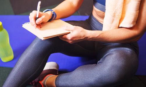 A woman in workout clothes writing down her fitness goals to make exercise intentional