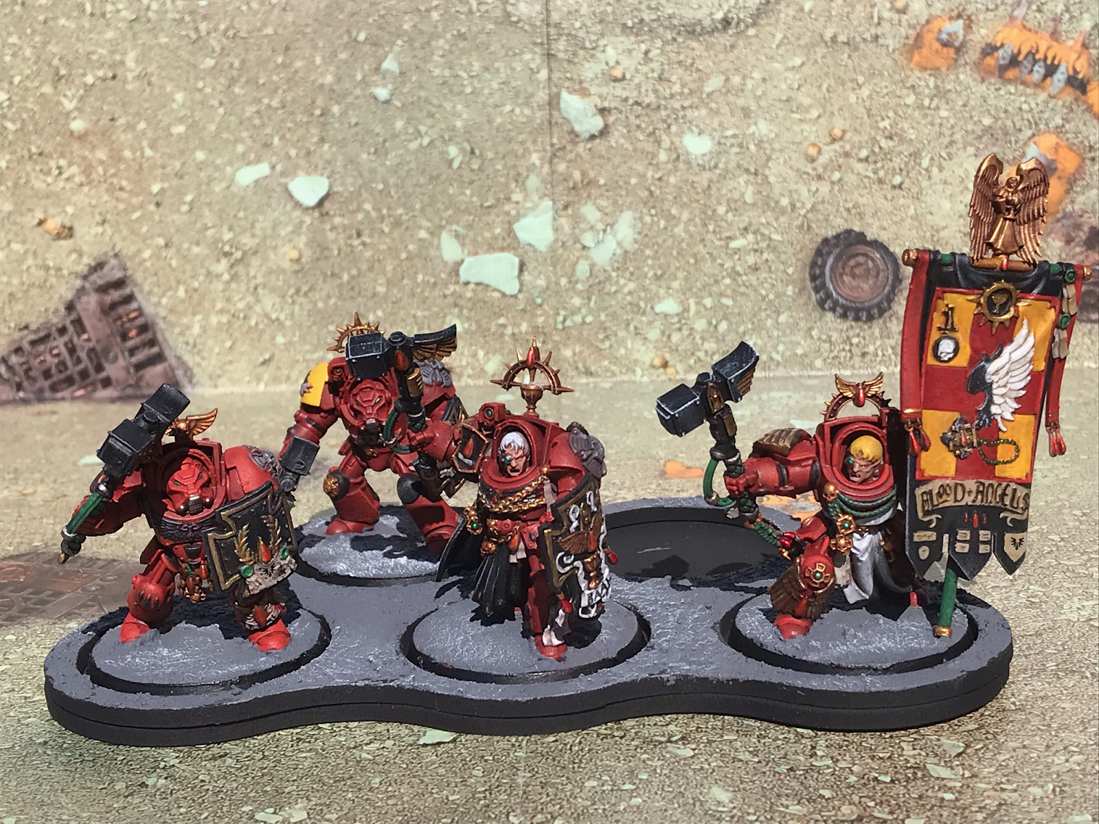 A unit of Blood Angels Terminators, heavily armoured warriors in red and gold. One carries a banner.