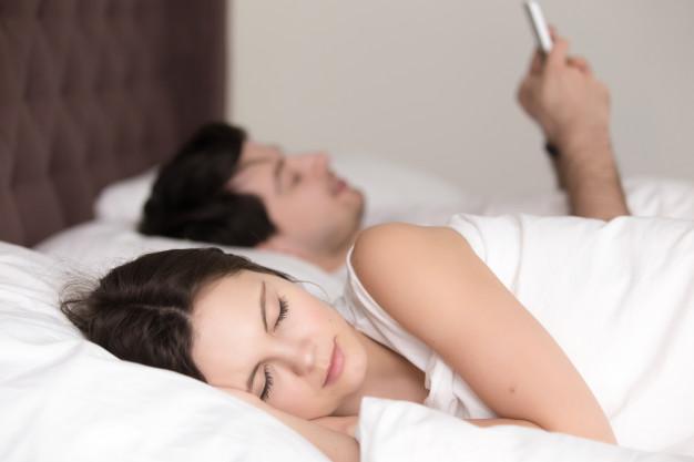 Jovem mulher dormindo enquanto seu namorado usando smartphone na cama Foto gratuita