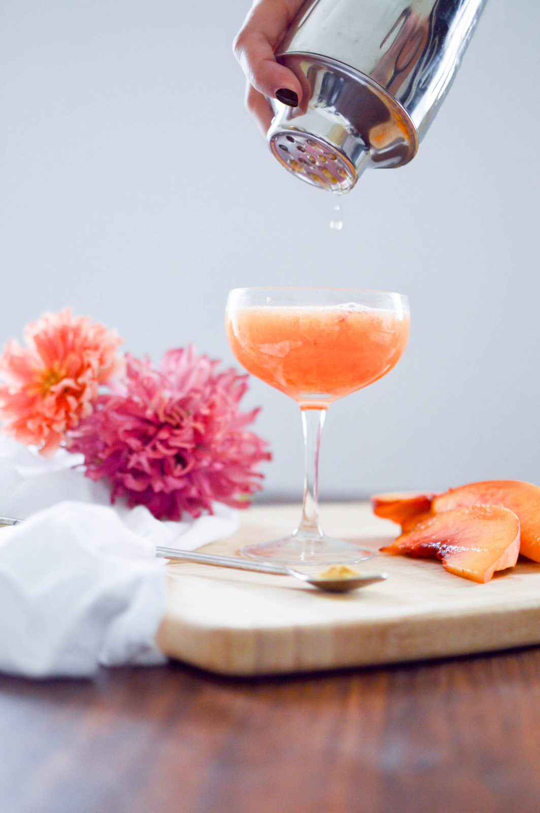 Taça com bellini dentro, uma bebida laranja. Também há três fatias de pêssego ao lado do drink. 