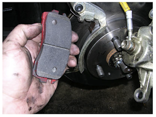 The repairperson is holding a set of brake pads, which need to be inspected for wear, and if too thin, must be replaced. If you ever hear a car's brakes squealing, it is because the brake pads are worn out.