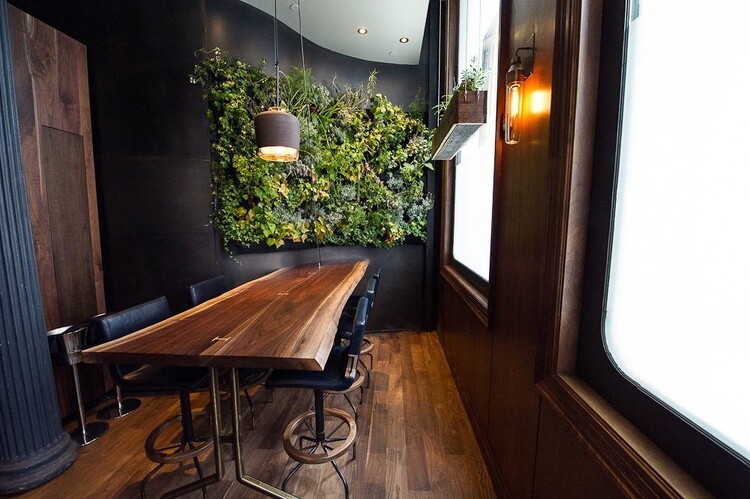 Bàn từ gỗ me tây kết hợp với ghế da, sàn và tường gỗ cùng cây xanh đem cảm hứng thiên nhiên vào tràn ngập căn phòng.