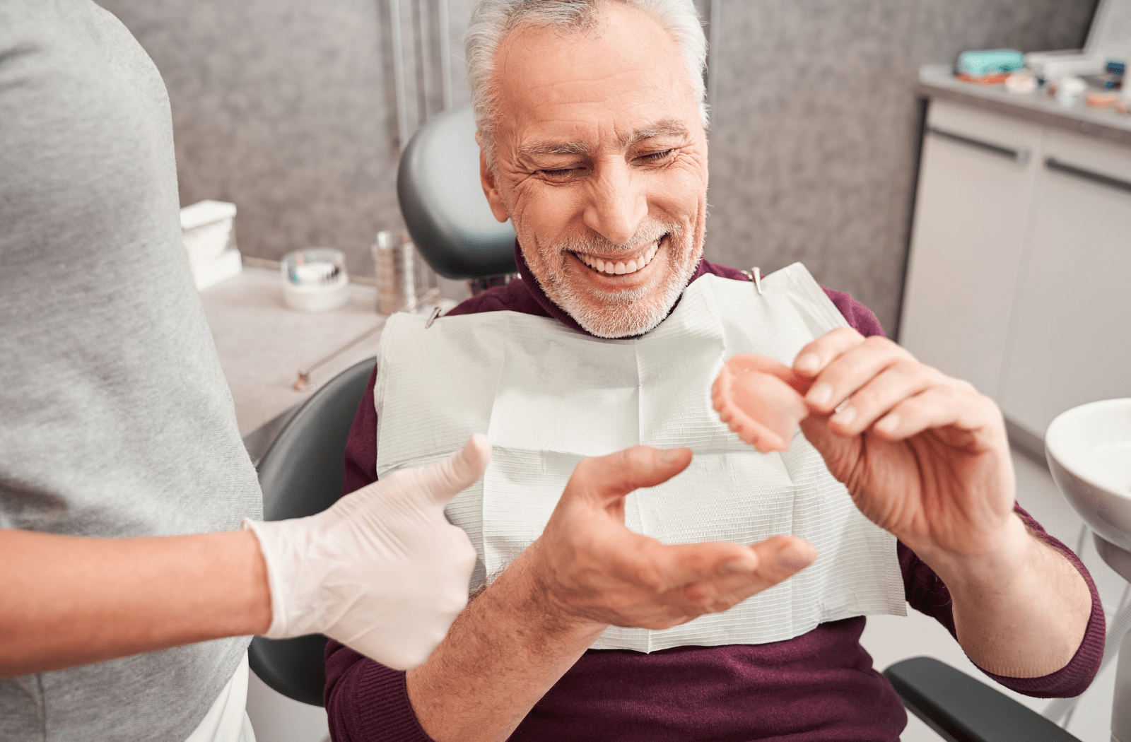 An older man at the dentist's office with a new top denture in his hand, and the dentist is giving a thumbs-up