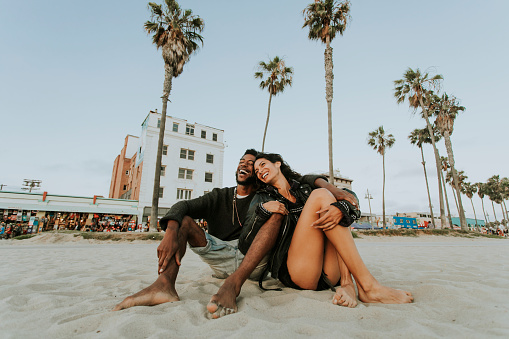 A mixed race, heterosexual couple sitting on a beach in California cuddling and smiling as they look at the beach. When your partner wants to know about past relationships. You can get couples therapy and marriage counseling in Los Angeles, CA with a licensed marriage counselor via online therapy in California here.  91364