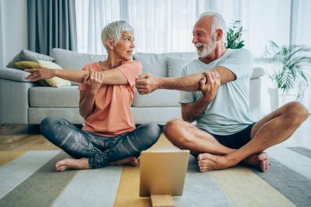 Couple exercising together at home. Beautiful mature couple sitting on the floor and practicing yoga. Sporty couple using digital tablet for online yoga lessons. elderly exercising stock pictures, royalty-free photos & images