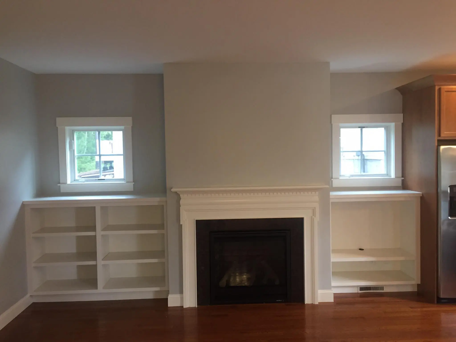 An undecorated living room with white shelves on each side of a fireplace.