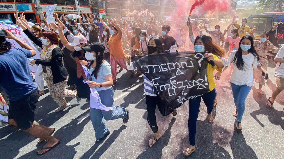 Women holding banners, emergency flare sticks and fire sticks as they march during a demonstration against the military coup in Yangon in July 2021
