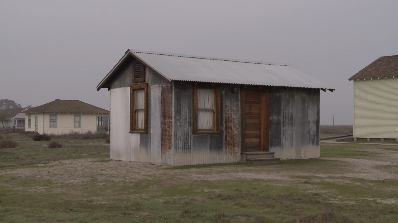 From the film ALLENSWORTH, a small shack sit on bare land, with other houses on either side. The shack is rusted and old.