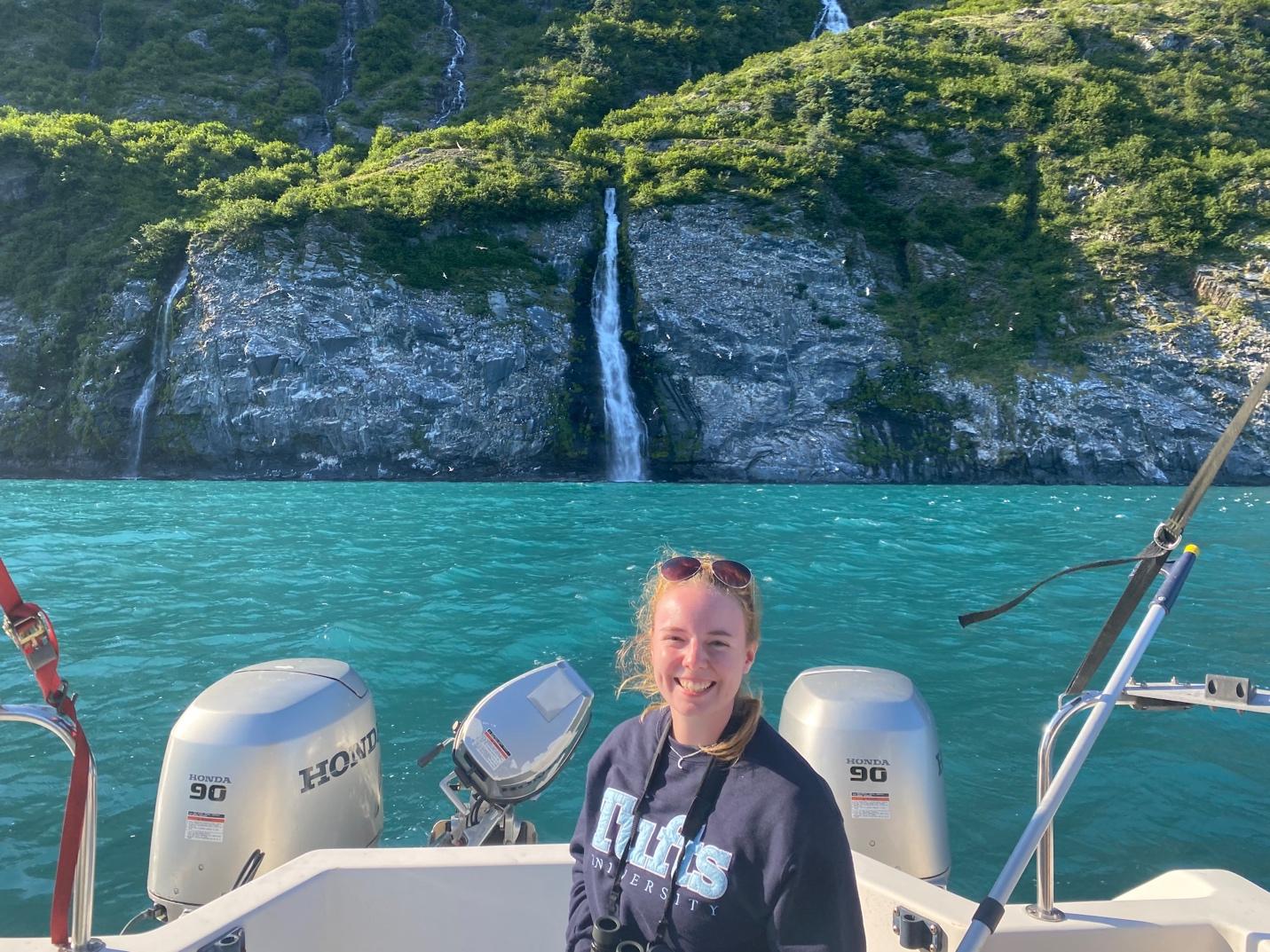 A person on a boat in front of a waterfall  Description automatically generated