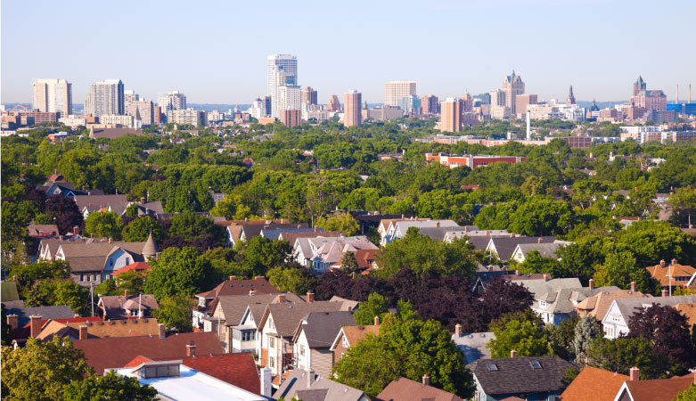 Residential homes interspersed with mature green trees on the north side of the city of Milwaukee, visible in the background