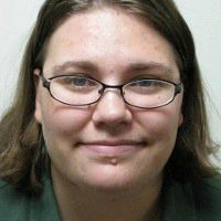 A woman with brown hair and glasses smiles into the camera