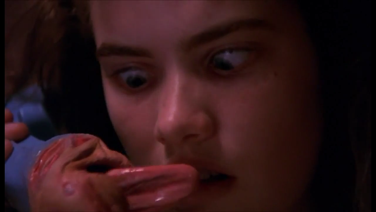 Screencap from the movie Nightmare on Elm Street. Nancy, a young dark haired white woman, is looking down at her phone in confused terror because the receiver now has lips and a tongue wagging at her.