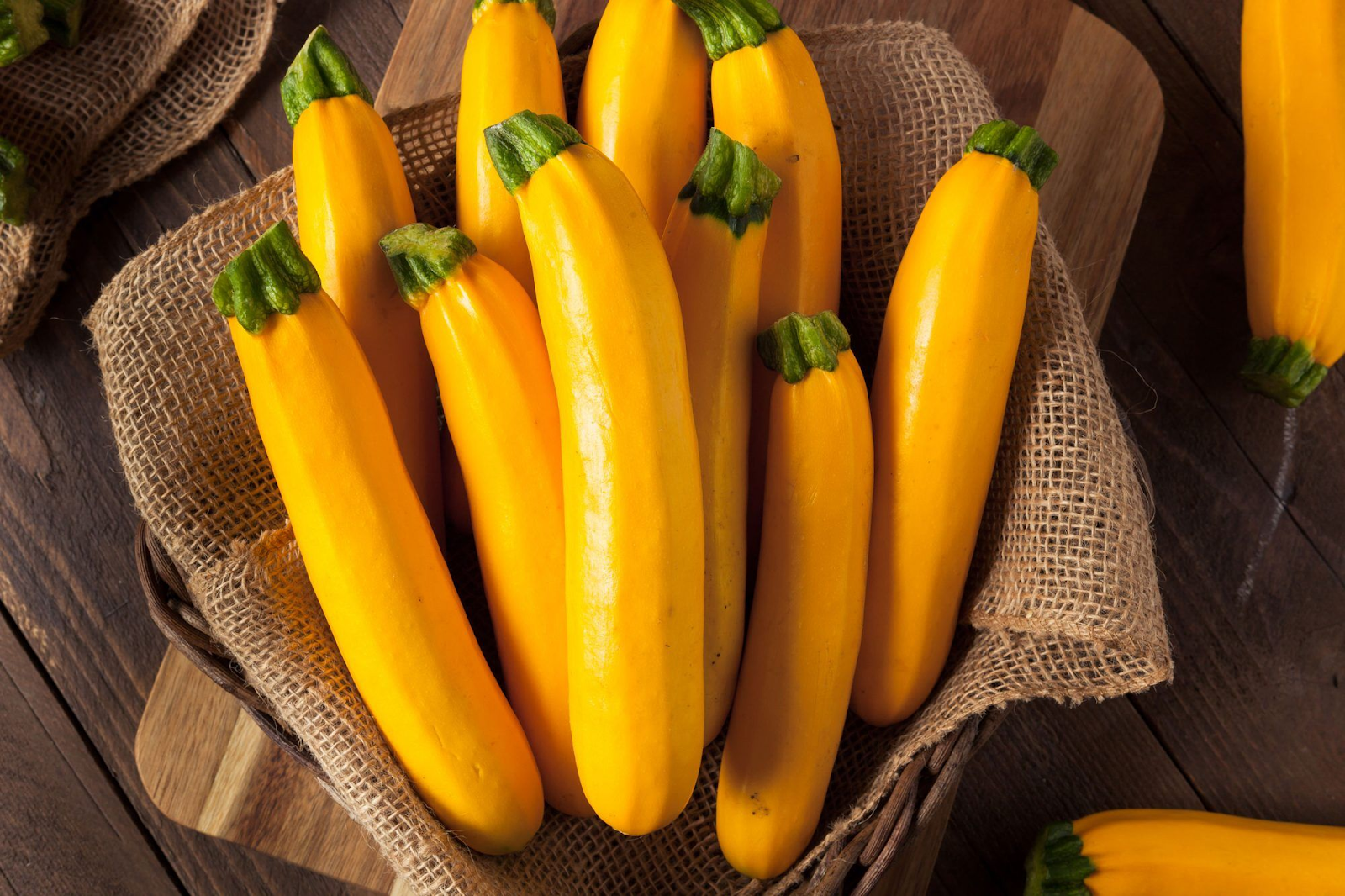 A close-up of a golden zucchini squash on a green plant with large leaves." This alt text provides a clear and concise description of the image, including the type of vegetable, its color, and the appearance of the plant it grows on