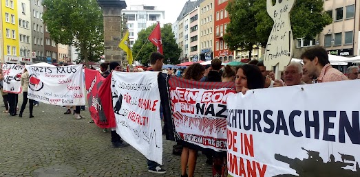 Demonstranten mit Transparenten u.a. Bild eines Panzers »Fluchtursachen made in Germany«.