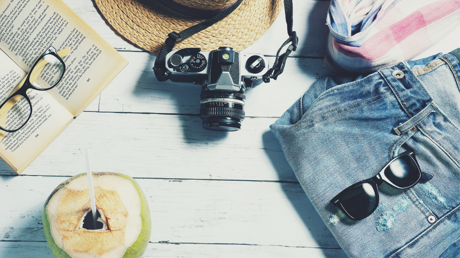 Camera, book, hat, shorts and sunglasses laid out on wooden flooring