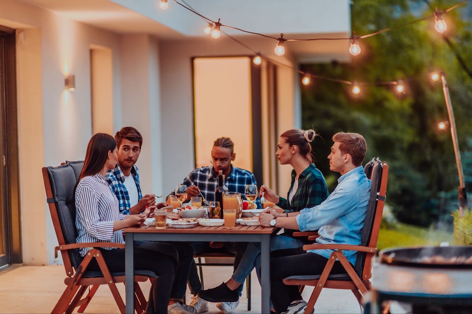 A group of friends sitting around a table at a backyard barbecue.