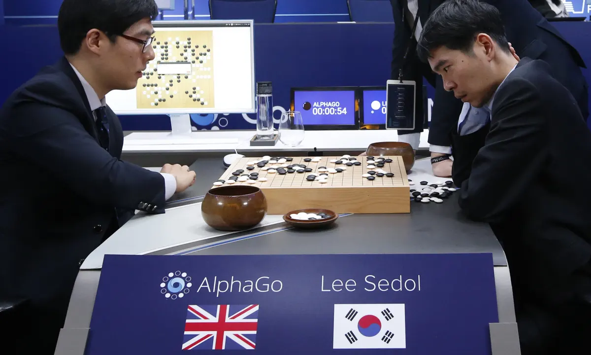 Lee Sedol (right) sits looking stressed as he fights against the AI machine 'AlphaGo', who devises the moves which are then enacted by a human operator (left). A Go board sits between them covered in white and black pieces