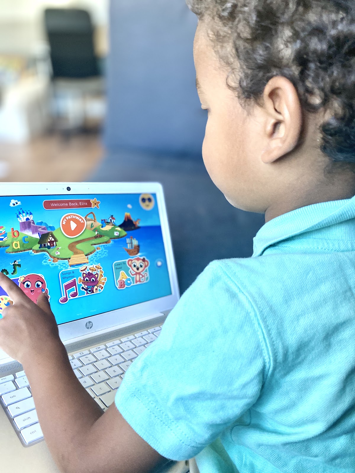 A little boy sits on a couch holding a computer while playing with the Homer reading app