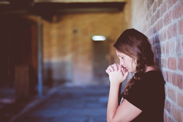 Woman praying in a dark corridor near a brick wall