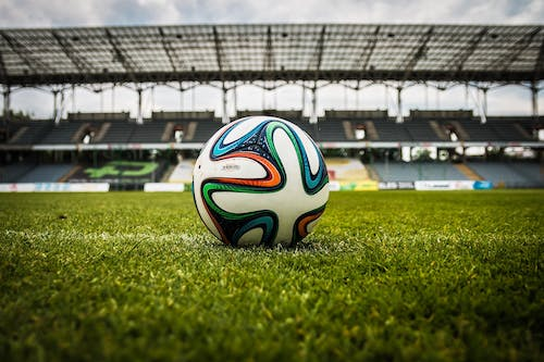 A soccer ball left on the center of the pitch in an empty stadium 