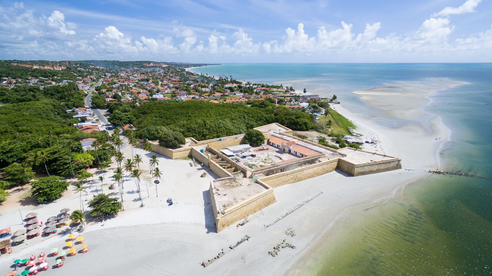 Imagem aérea do Forte Orange/Fortaleza de Santa Cruz. Parte da Praia do Forte ao lado esquerdo da foto, com larga faixa de areia em frente ao mar cristalino e esverdeado.

