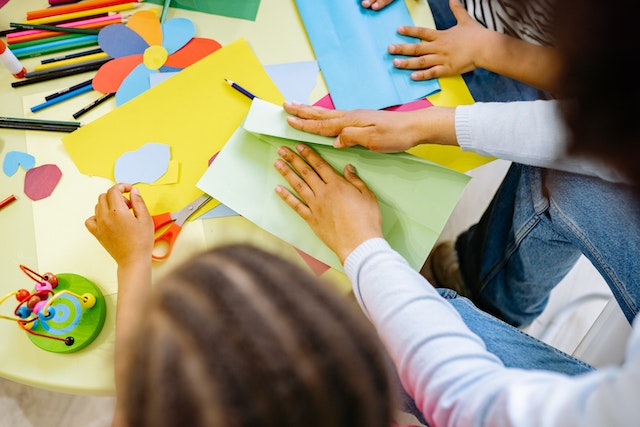 children sitting at a table with color paper working on arts and crafts
