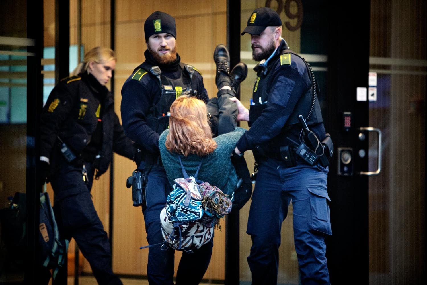 Two police officers carry out a young rebel from the Total HQ, each officer holding one arm and one leg