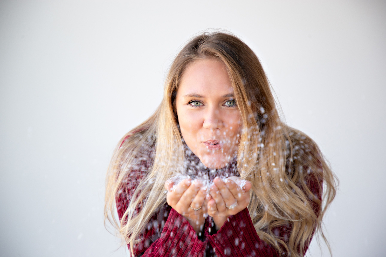 fun christmas card pose of girl blowing snow at the camera in a red turtleneck