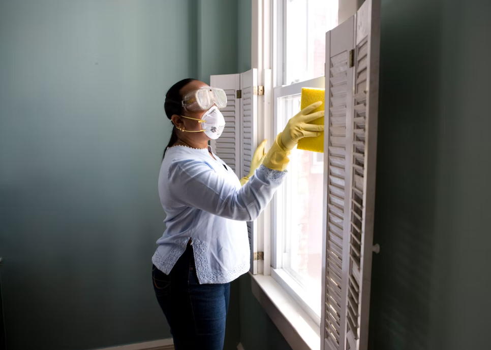 Woman in protectant gear cleaning the disinfecting the window