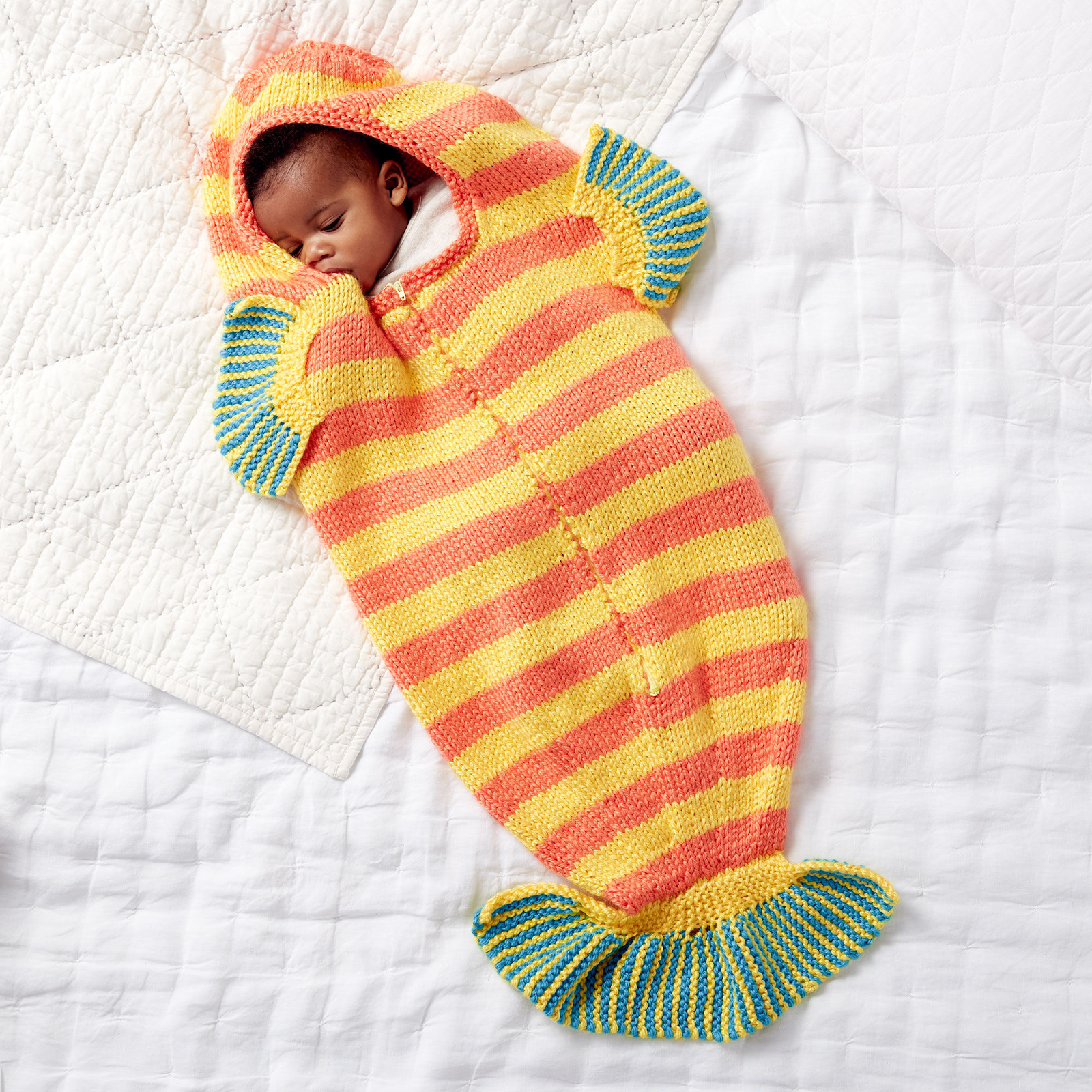 baby sleeping in a sleep sack that has stripes and fins
