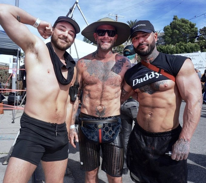 Danny Starr posing for a photo with friends outside while wearing a black daddy crop top and smiling for the camera