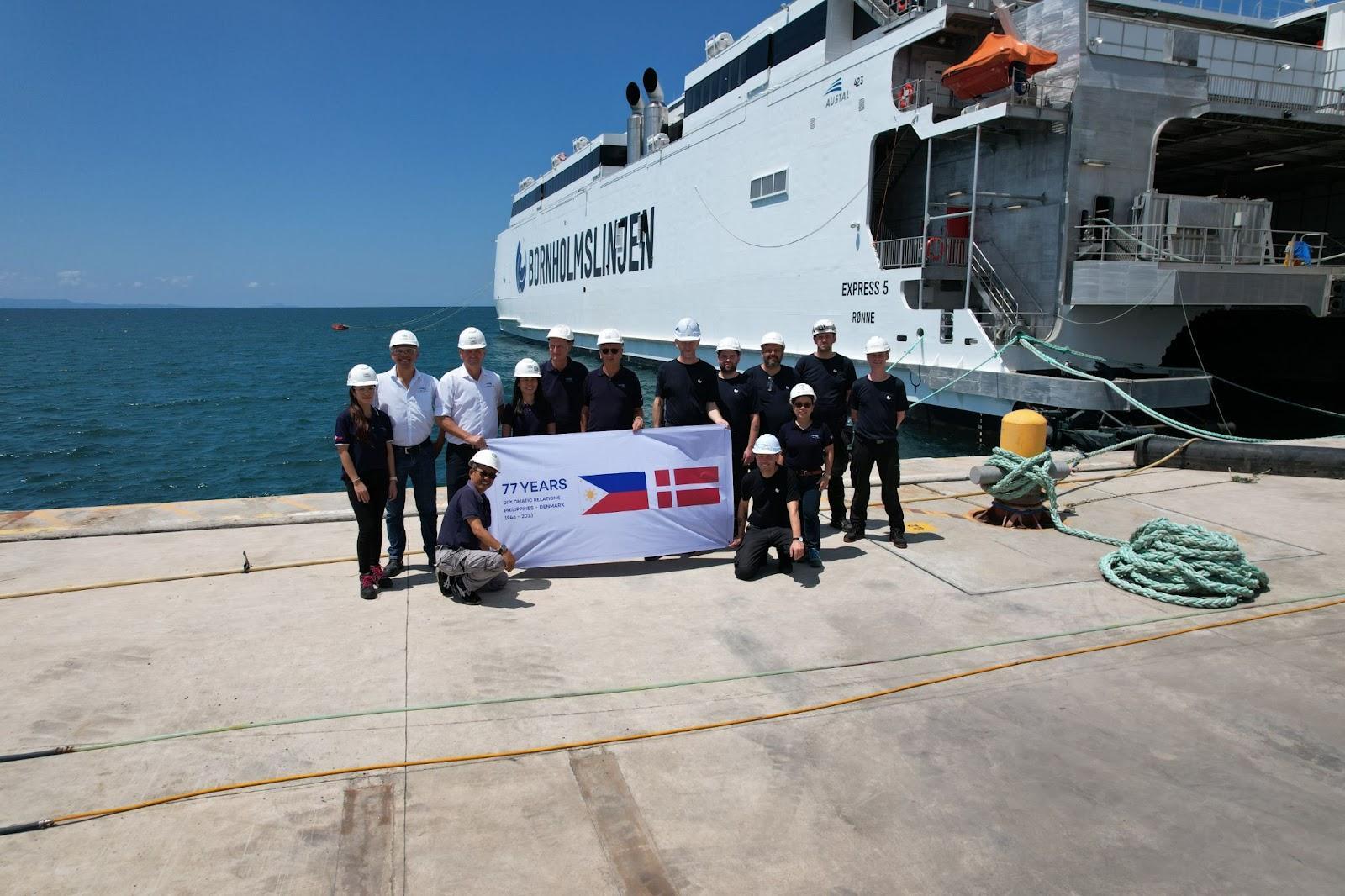 A group of people standing on a dock with a signDescription automatically generated with low confidence