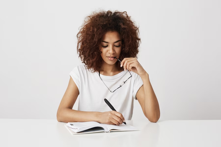 a girl holding eyeglasses and writing on a notebook