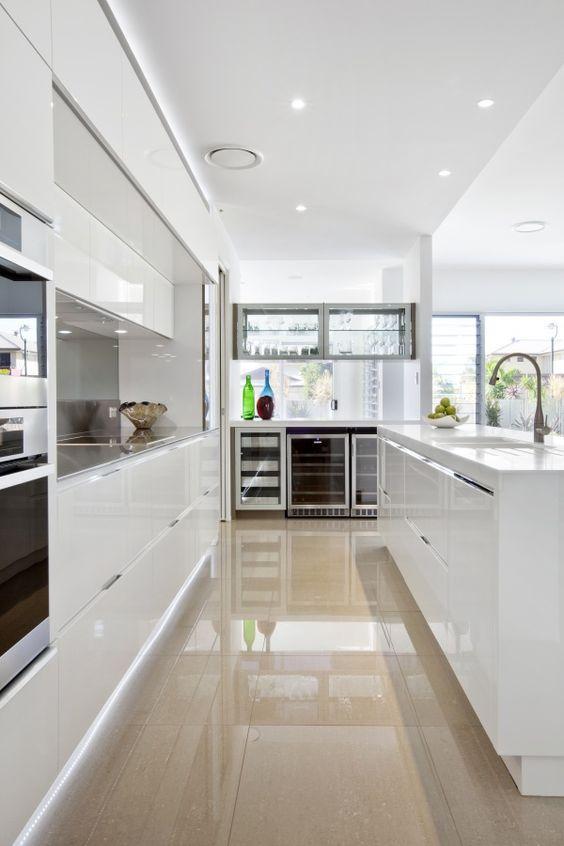 Cozinha com mobília branca, porcelanato em tom neutro no piso, eletrodomésticos de inox e paredes brancas.