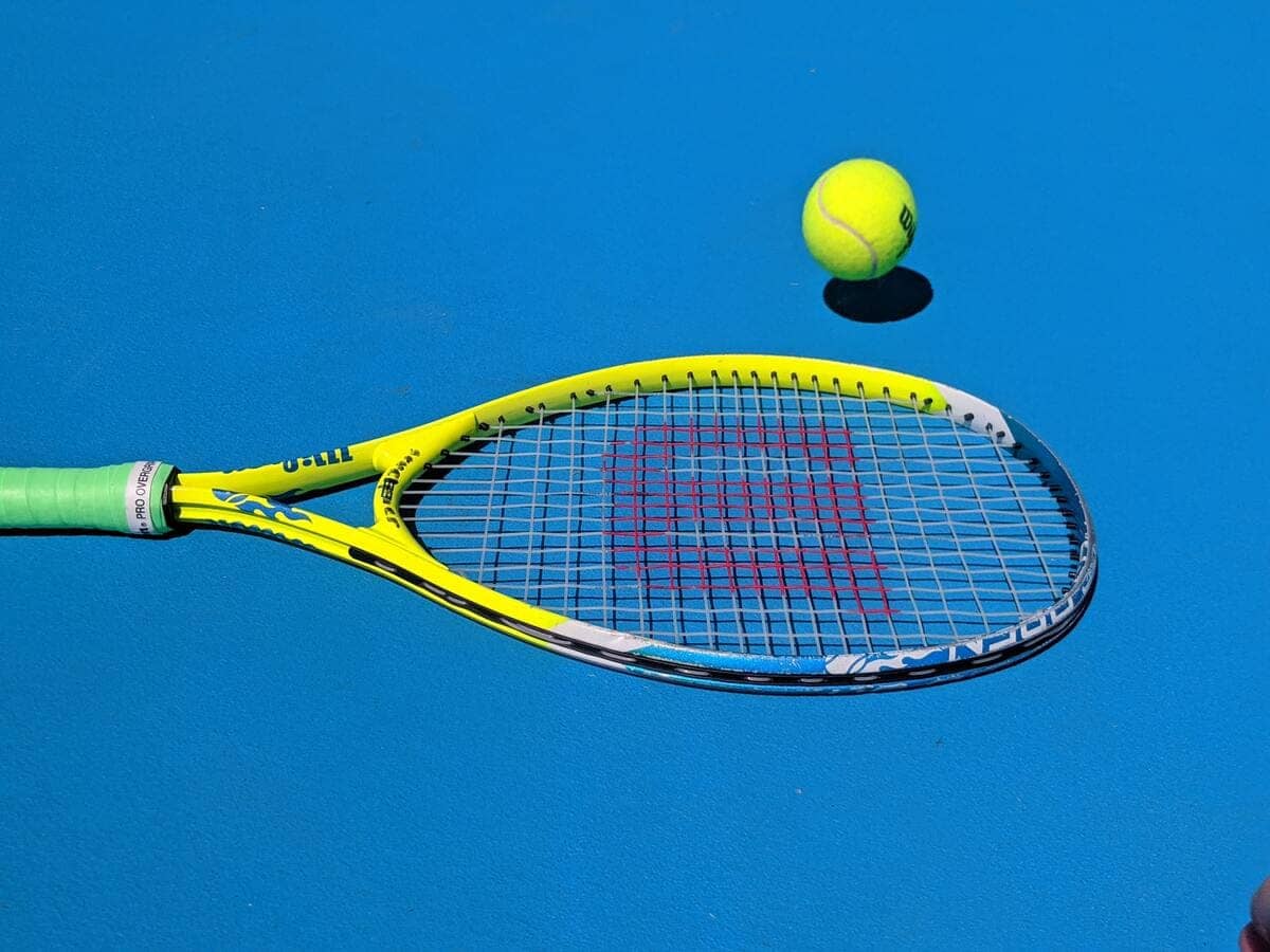 Una racchetta da tennis Wilson e una pallina su una superficie blu