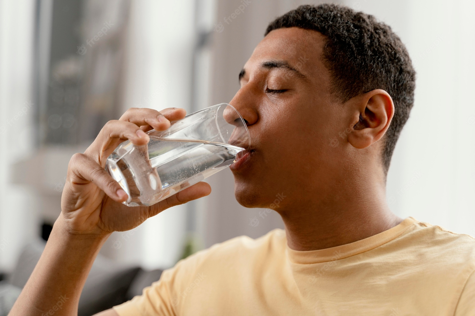 Homem negro de camiseta amarela está com os olhos fechados e bebe água