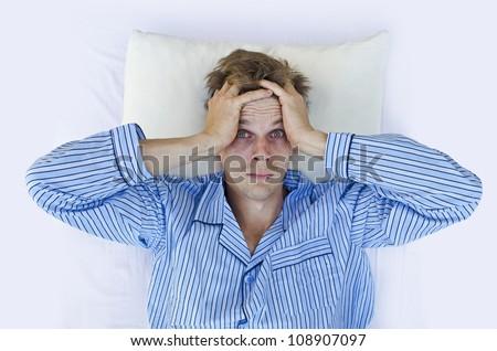 A man lying awake on a bed with red eyes while holding his head